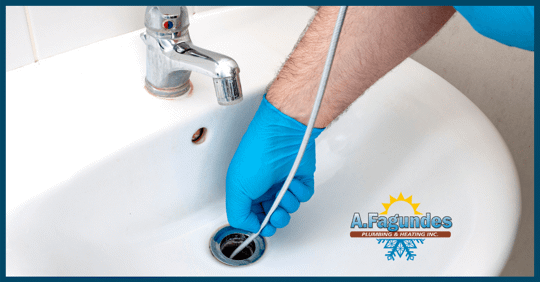 Photo of a plumber wearing a bright blue glove snaking a sink drain