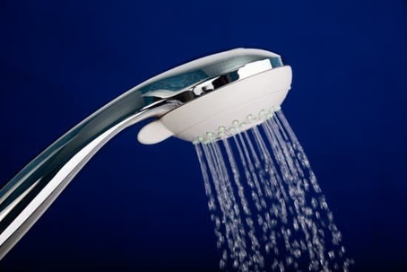A metal showerhead with water coming out against a navy backdrop