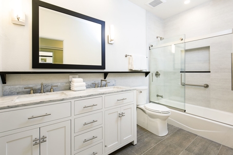 A remodeled bathroom complete with wood floors, white cabinets, dual sinks, a toilet, a shower, and a mirror